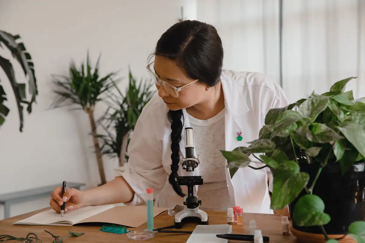 Cercetătoare care își notează observațiile lângă un microscop și plante